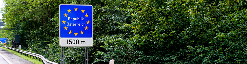 Straßenschild mit EU-Sternen und der Aufschrift 'Republik Österreich', 1500 Meter vor der österreichischen Grenze, umgeben von grüner Natur